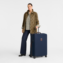 Load image into Gallery viewer, A person standing next to the Longchamp Boxford Suitcase Embossed Style xl blue - suitcase reaches her mid thighs