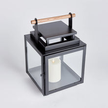 Load image into Gallery viewer, black metal lantern with glass sides and wood handle on the top of the lantern