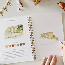 Load image into Gallery viewer, Farm Watercolor Workbook with a person painting farm land