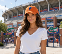 Load image into Gallery viewer, A woman stands outdoors in front of Florida State Stadium wearing an orange baseball cap with a blue letter 'F' and a white V-neck t-shirt.