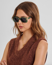 Load image into Gallery viewer, A woman with wavy light brown hair wearing green square sunglasses with gold accents and a brown fuzzy sleeveless top, photographed against a light gray studio background.