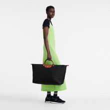 Load image into Gallery viewer, Person carrying Longchamp Le Pliage Original Large Luggage Travel Bag in black and holding the bag by the small center handles.