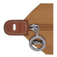 Load image into Gallery viewer, Person carrying Longchamp Le Pliage Original Large Luggage Travel Bag in fawn - close up of zipper pull with Longchamp logo