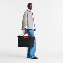 Load image into Gallery viewer, person holding a partly expanded expanded Longchamp Le Pliage Original Travel Bag in Black canvas and brown leather