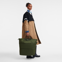 Load image into Gallery viewer, person holding the fully expanded Longchamp Le Pliage Green Travel Bag Expandable in Forest green
