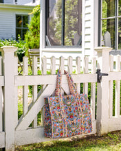 Load image into Gallery viewer, Printfresh Bee Tapestry Traveler Tote in a colorful print with bees. Bag is hung on a white picket fence gate