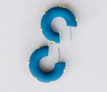 Load image into Gallery viewer, A pair of chunky, curved C-shaped hoop earrings in a vibrant blue color, embellished with small gold studs along the outer edge, displayed on a clean white background.