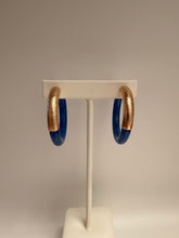 Load image into Gallery viewer, Two gold and blue rings hanging on a white hook against a beige background