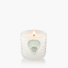 Load image into Gallery viewer, A lit VOLUSPA Garden Vanilla Voltage scented candle in a ribbed translucent white glass jar, centered against a clean white background.