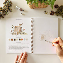 Load image into Gallery viewer, Woodland Watercolor Workbook with person painting a tree stump with bird