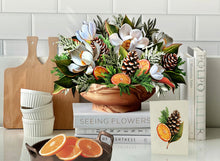 Load image into Gallery viewer, FreshCut Paper Winter Magnolia Greeting Card on a stack of books