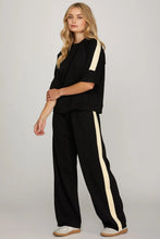 Load image into Gallery viewer, woman wearing black pants and shirt with cream colors accents along the side of the sleeves and the side of the pants
