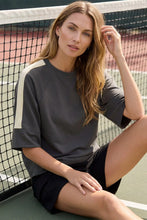 Load image into Gallery viewer, woman on a tennis court wearing charcoal  shirt with cream colors accents along the side of the sleeves 
