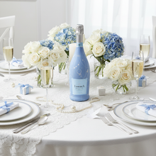 Load image into Gallery viewer, Champagne Bottle covered with the Blue Pearls &amp; Prosecco Prosecco Bottle Wrap on a table set for a wedding with white and blue flowers
