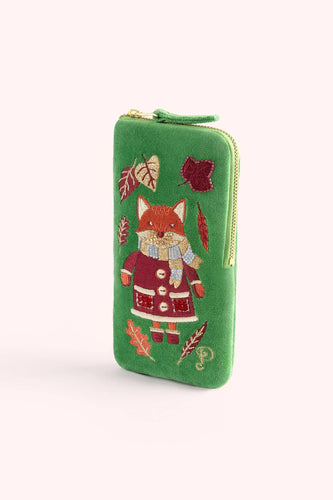 green velvet sunglasses case with embroidered fix wearing a coat and scarf surrounded by fall leaves