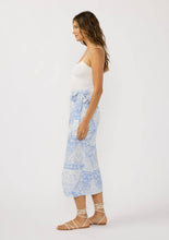 Load image into Gallery viewer, person wearing a blue and white wrap skirt paired with a white tank top and white sandals  side view showing bow tied at the waist

