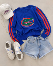 Load image into Gallery viewer, Florida Gators AirKnit Long Sleeve Blue Sweater with the gator logo and orange stripes on the arms paired with a gator hat, jean shorts and runners

