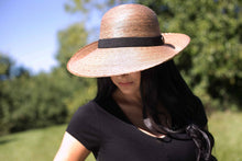 Load image into Gallery viewer, woman wearing the Chloe Hand-woven Palm Hat outdoors in the sun
