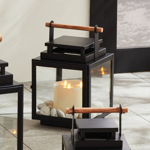 black metal lantern with glass sides and wood handle on the top of the lantern