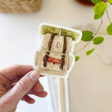 Load image into Gallery viewer, Hand holding a Camp Backpack Sticker in a watercolor style
