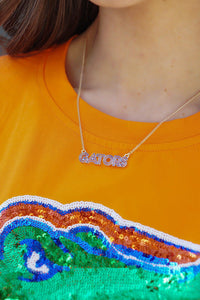 person in gator t-shirt wearing a necklace with a pendant that reads Gators in orange and blue enamel  