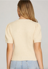Load image into Gallery viewer, A woman viewed from the back wearing a cream-colored short-sleeve knit top with puffed shoulders and light blue jeans, set against a plain light gray studio background.
