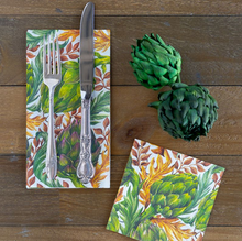 Load image into Gallery viewer, Two decorative paper napkins with a botanical artichoke print are arranged on a rustic wooden table. One napkin is folded and placed under a fork and knife, while the other napkin lies flat beside it.
