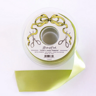 A spool of Heritage Cook 'Fancy Sage Ribbon' with pale sage green ribbon unspooled below, shown on a clean white background.