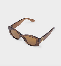 Load image into Gallery viewer, A pair of designer sunglasses with a translucent dark brown acetate frame and warm brown lenses, featuring gold-tone 'BAZAAR' branding on the temples, set against a light gray background.
