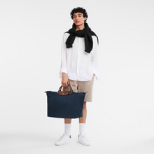 Load image into Gallery viewer, Person carrying Longchamp Le Pliage Original Large Luggage Travel Bag  in navy and holding the bag by the small center handles.
