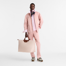 Load image into Gallery viewer, person holding the Longchamp Le Pliage Original X-Large Travel Bag in paper by the two handles 
