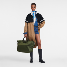 Load image into Gallery viewer, person holding partly expanded Longchamp Le Pliage Green Travel Bag Expandable in Forest green
