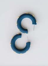 Load image into Gallery viewer, A pair of chunky, curved C-shaped hoop earrings in a matte navy blue finish, accented with small gold studs along the outer edge, shown on a light gray background.
