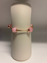 Load image into Gallery viewer, Gold bracelet with pink beads on a cylindrical white stand against a gray background
