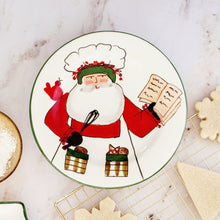Load image into Gallery viewer, Vietri Old St. Nick 2025 Limited Edition Salad Plate Santa in a chef hat holding a whisk and reading from a book. The plate is sitting on a countertop with cookies

