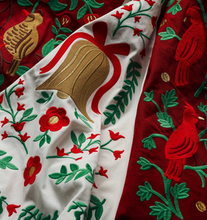 Load image into Gallery viewer, Close-up of a richly embroidered textile featuring a white section with red flowers, green leaves, and a gold bell motif, alongside a deep red section with red birds and green foliage.
