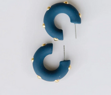 Load image into Gallery viewer, A pair of curved, C-shaped hoop earrings in a matte dark teal blue, accented with small gold studs along the outer edge, shown on a plain light gray background.
