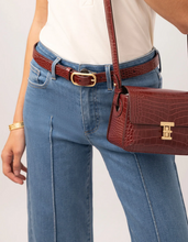 Load image into Gallery viewer, A close-up of a person wearing blue jeans, a white top, a brown crocodile-embossed belt, and a matching brown crocodile-embossed crossbody handbag with gold-tone hardware.
