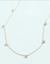 Load image into Gallery viewer, A delicate gold chain necklace featuring five small, evenly spaced round bezel-set clear gemstones on a pale light blue background.
