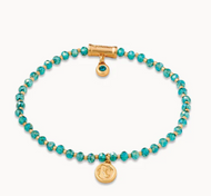 stone bracelet with teal stones interspersed with gold beads. A gold charm and large barrel shaped bead with dangling accent decorate the bracelet 