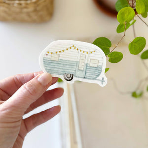 hand holding a blue and white camper trailer sticker in a watercolor style 