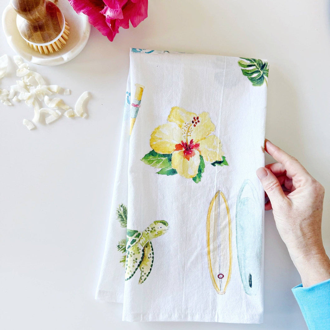 a hand holding white tea towel with tropical flower, sea turtle and surfboard designs in a watercolor style 