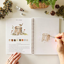 Load image into Gallery viewer, Woodland Watercolor Workbook with person painting a tree stump with bird

